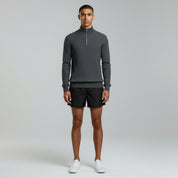 man wearing dark grey quarter zipped sweater and shorts on a plain background